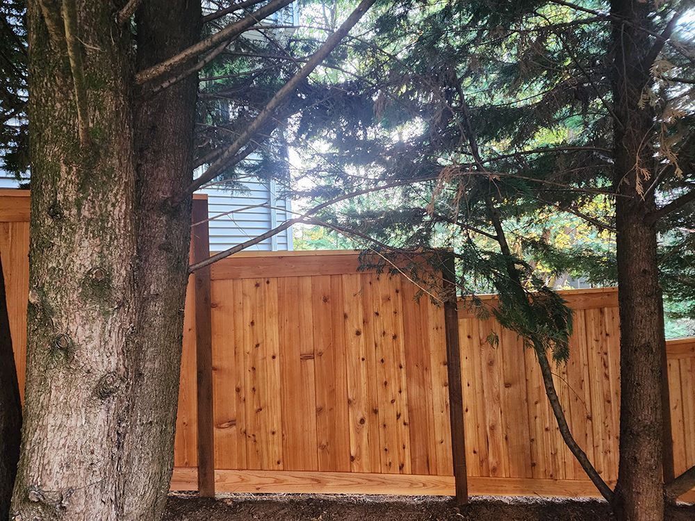 A wooden fence is surrounded by trees and a house