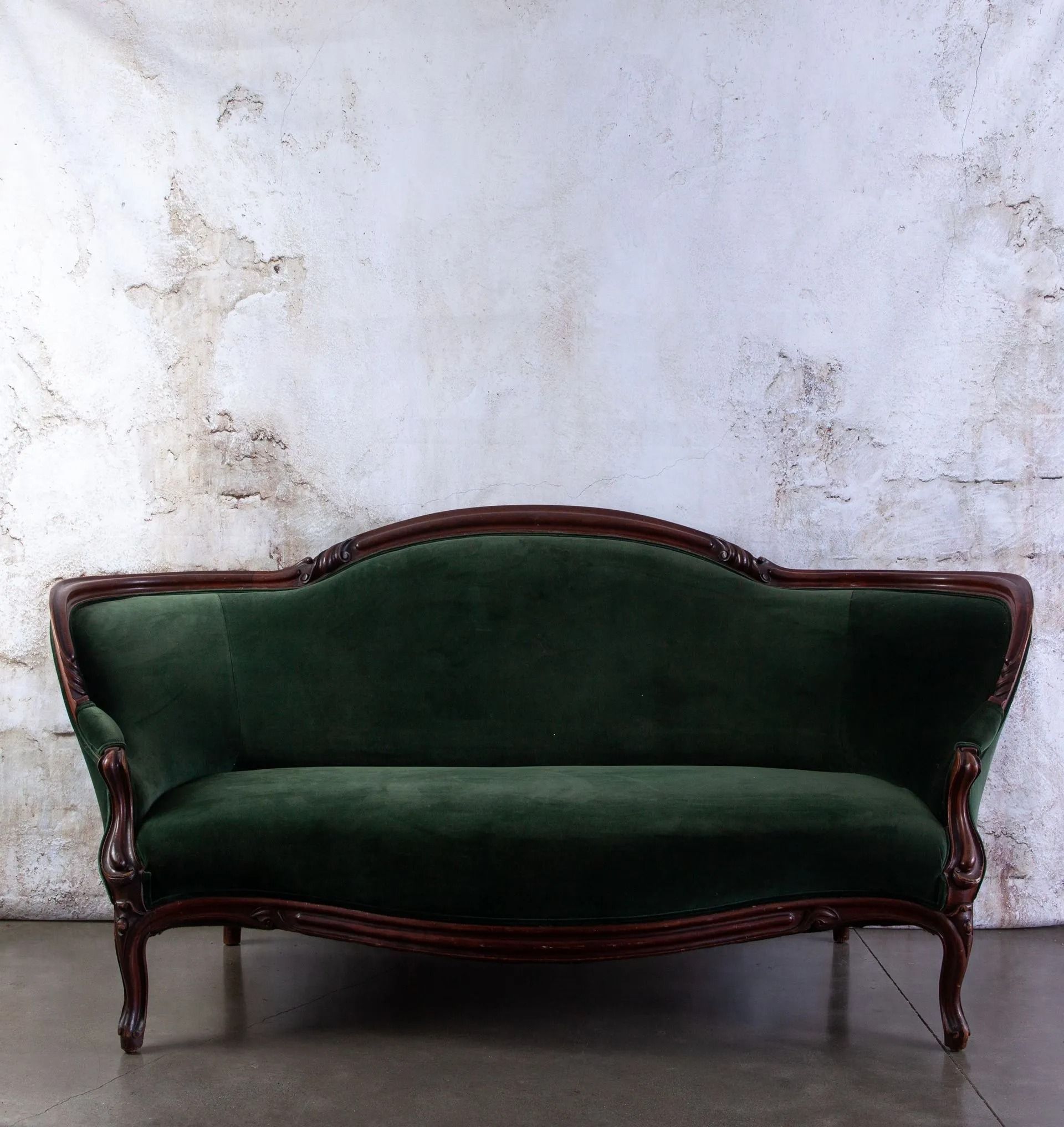 Dark green velvet sofa with mahogany trim against a mottled white wall.