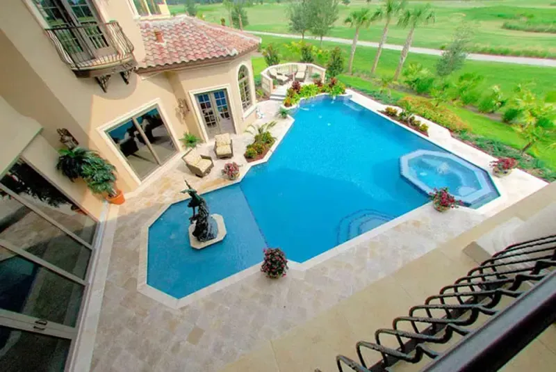 An aerial view of a large swimming pool with a hot tub in front of a house.