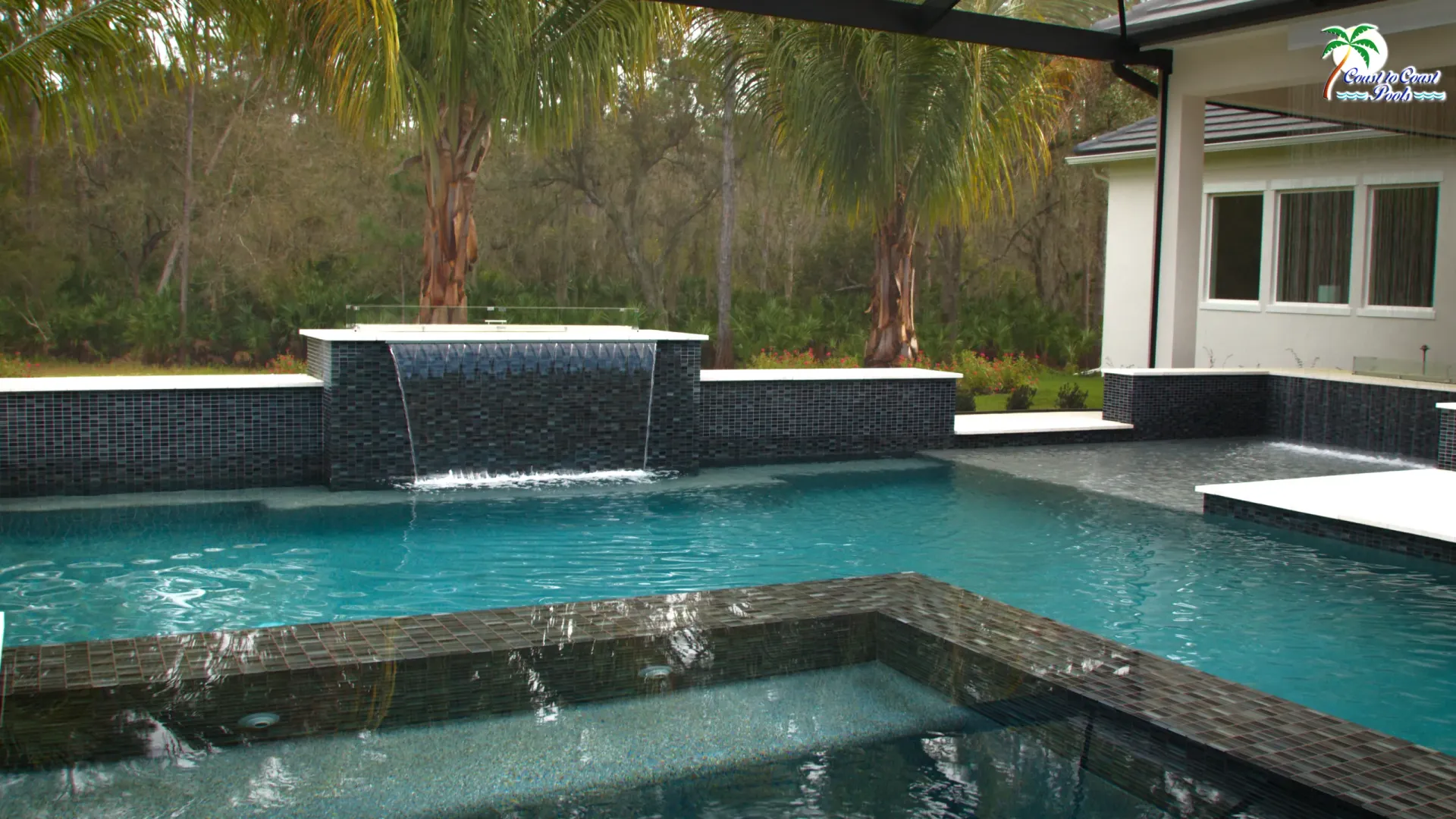 A large swimming pool with a waterfall in the backyard of a house.