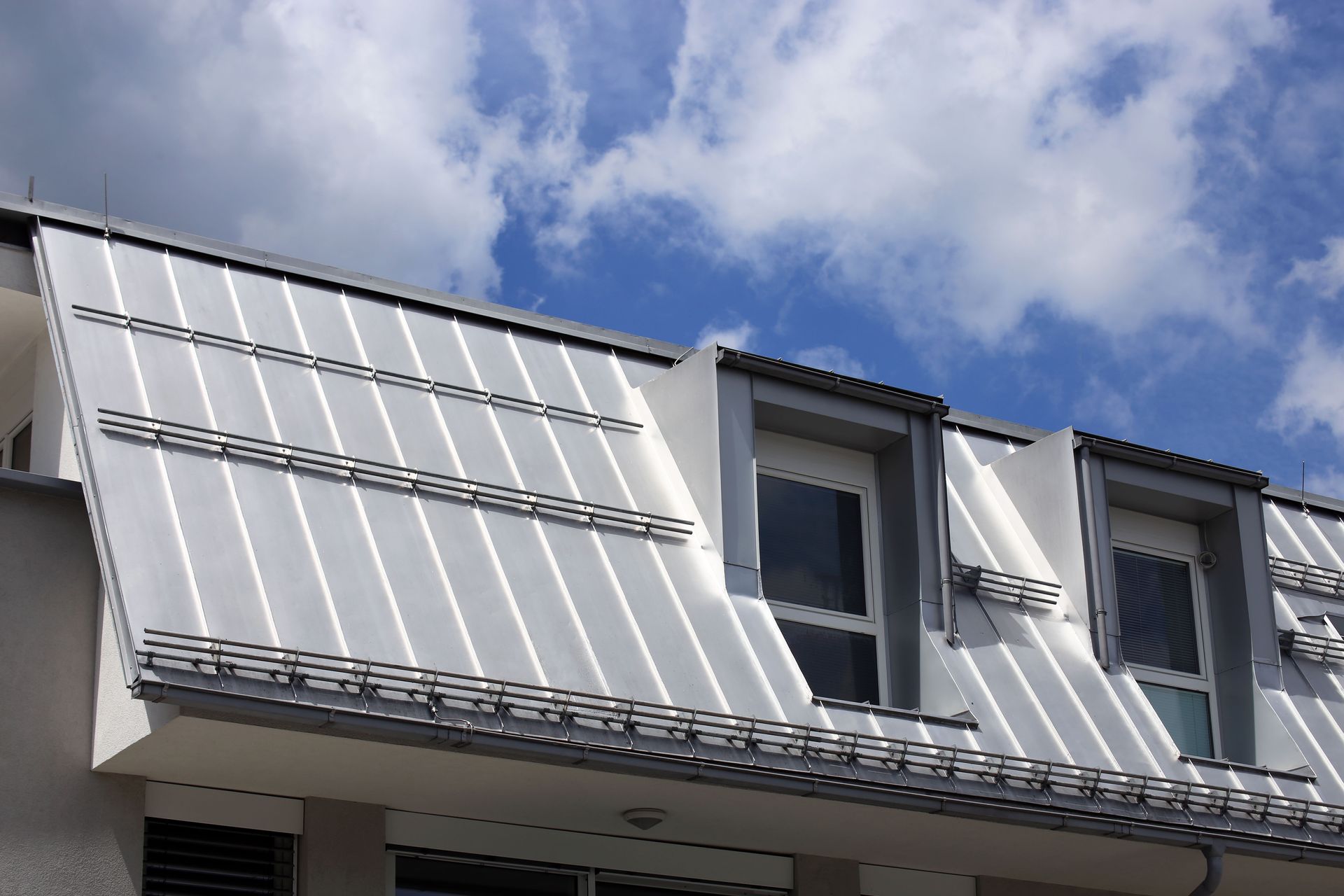 White metal roof with dormer windows, set against a partly cloudy blue sky.