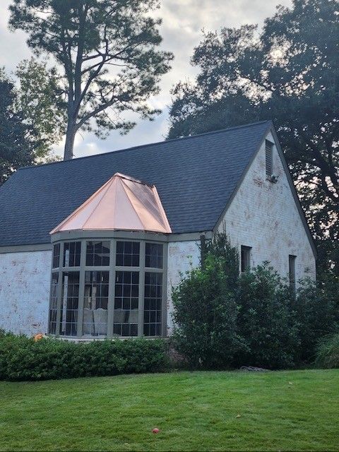 Cottage with a dark roof and copper accent, large window bay, stucco exterior, and green lawn.