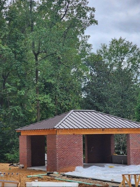 Brick pavilion with a metal roof surrounded by trees.