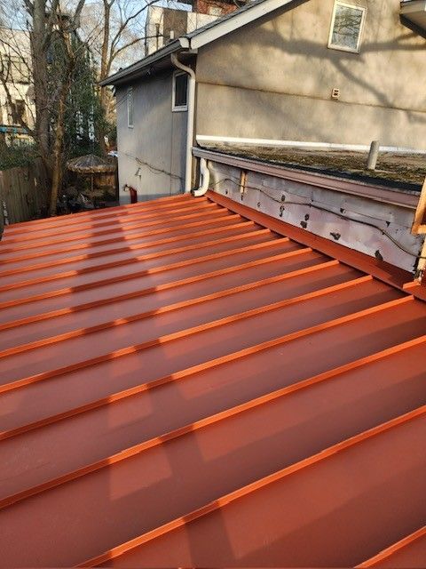 Red metal roof with vertical seams. Building exterior in the background.