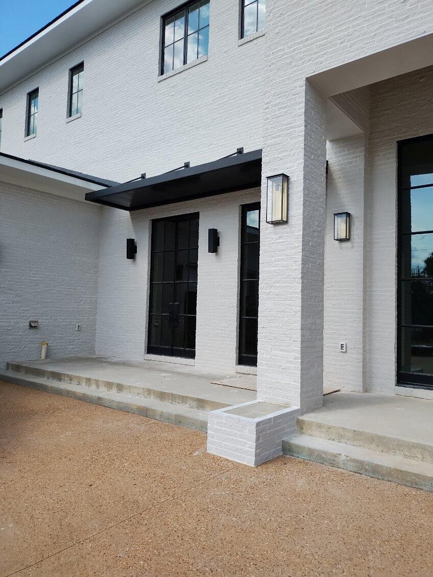 Exterior of a two-story modern home with white brick and black framed doors and windows.