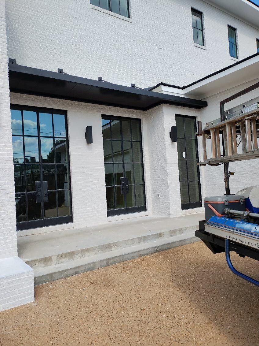 White stucco house with black framed windows and doors. Gravel yard, ladder visible.
