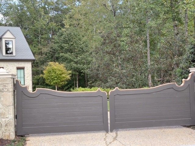 Gray wooden gates with ornate tops, leading to a house and trees.