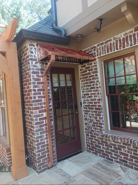 Brick building with a copper-roofed door awning, glass-paneled door, and a window with a brown frame.