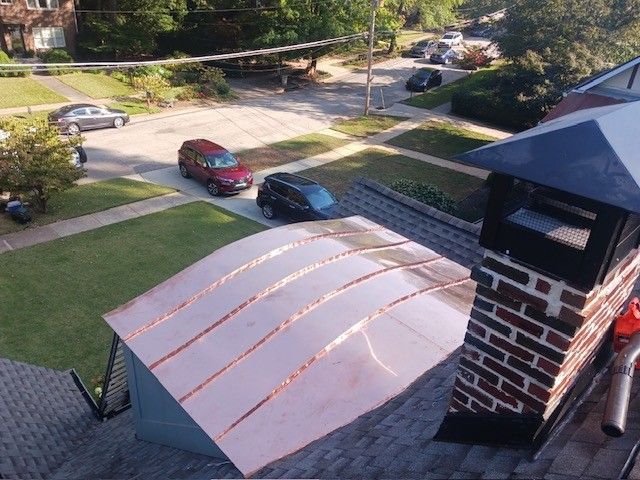 Copper roof section on a brick chimney; view of a residential street with cars and green lawns.