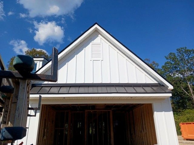 White house gable with black trim, blue sky, and unfinished garage entrance.