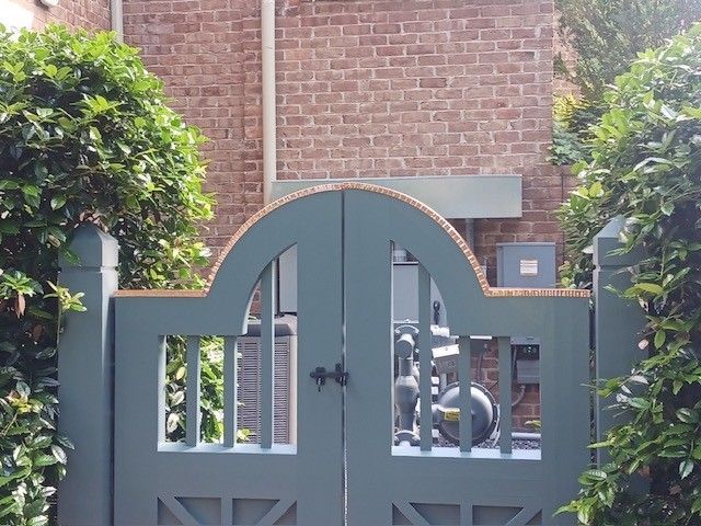 Green arched wooden gate in front of a brick wall, flanked by green bushes.