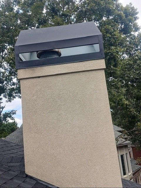 Beige chimney with a black cap on a dark roof, against a leafy background.