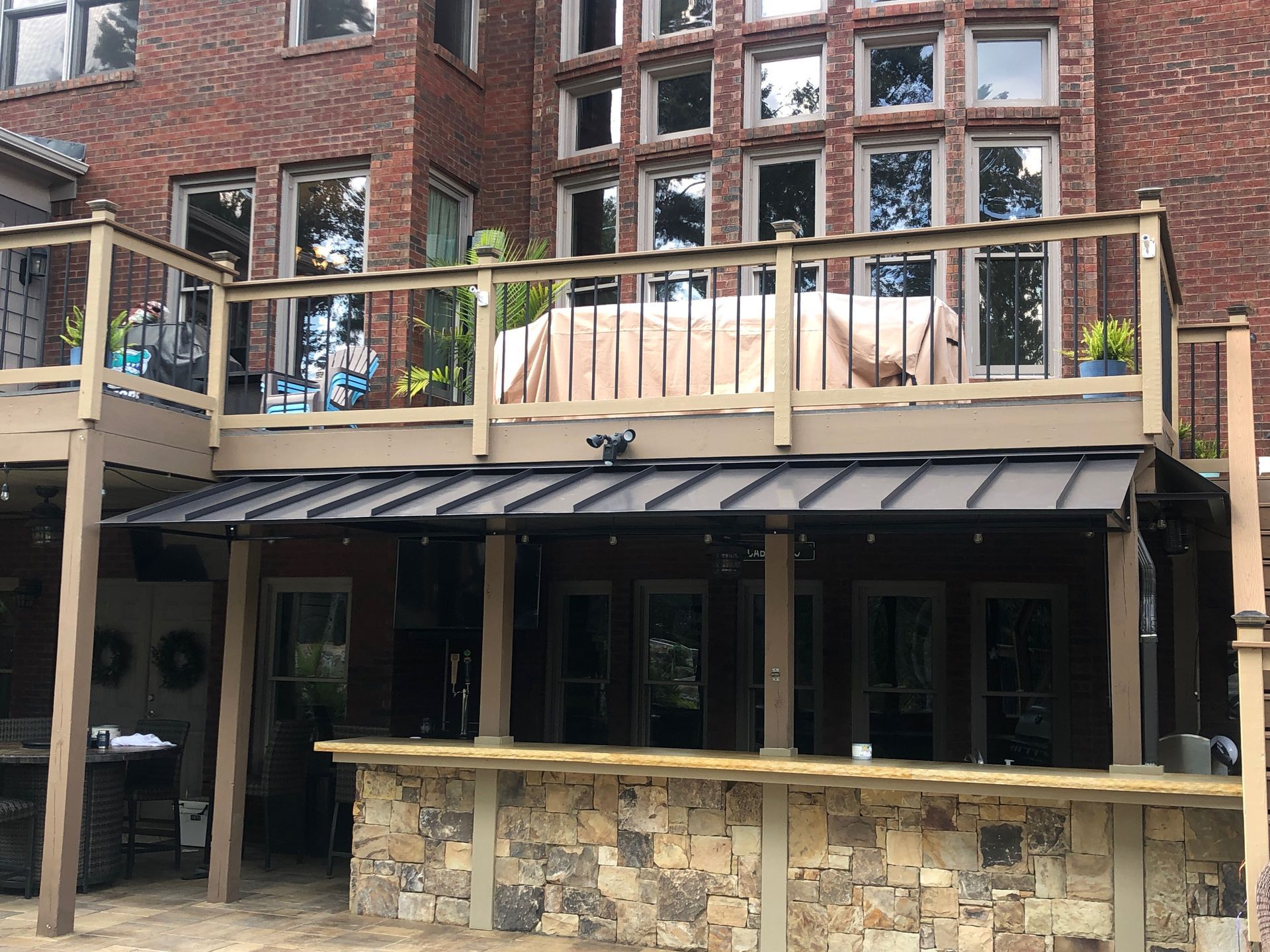 Two-story deck with a stone bar, a dark metal roof, and a brick house in the background.