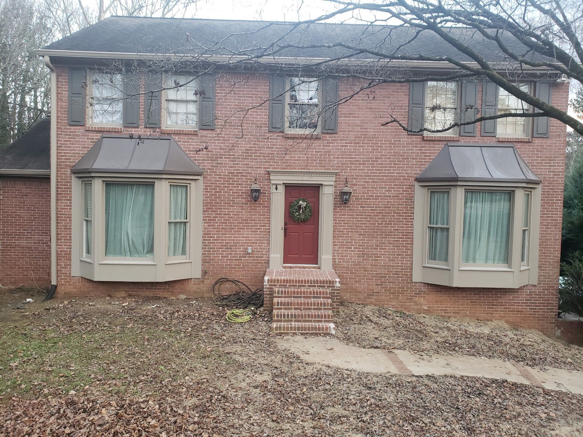 Red brick two-story house with brown shutters and bay windows; front door with wreath.