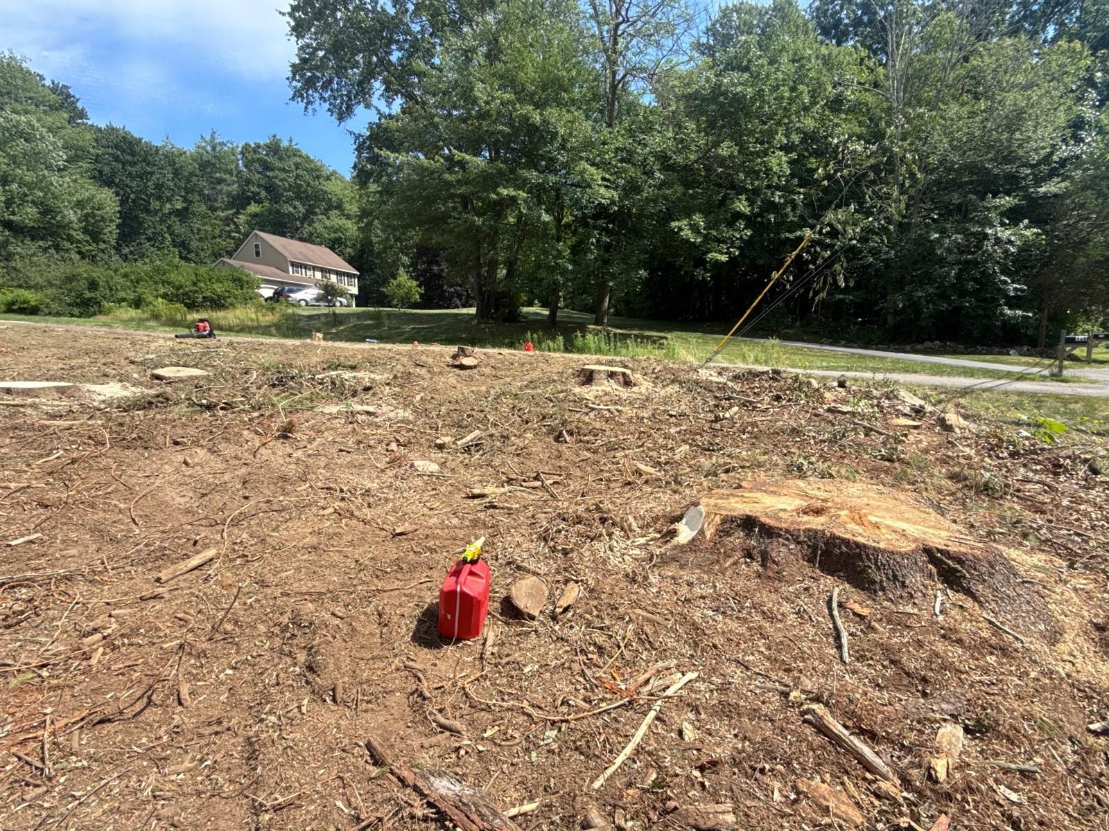 Cleared dirt lot with a red gas can in the foreground, trees and a house in the background.