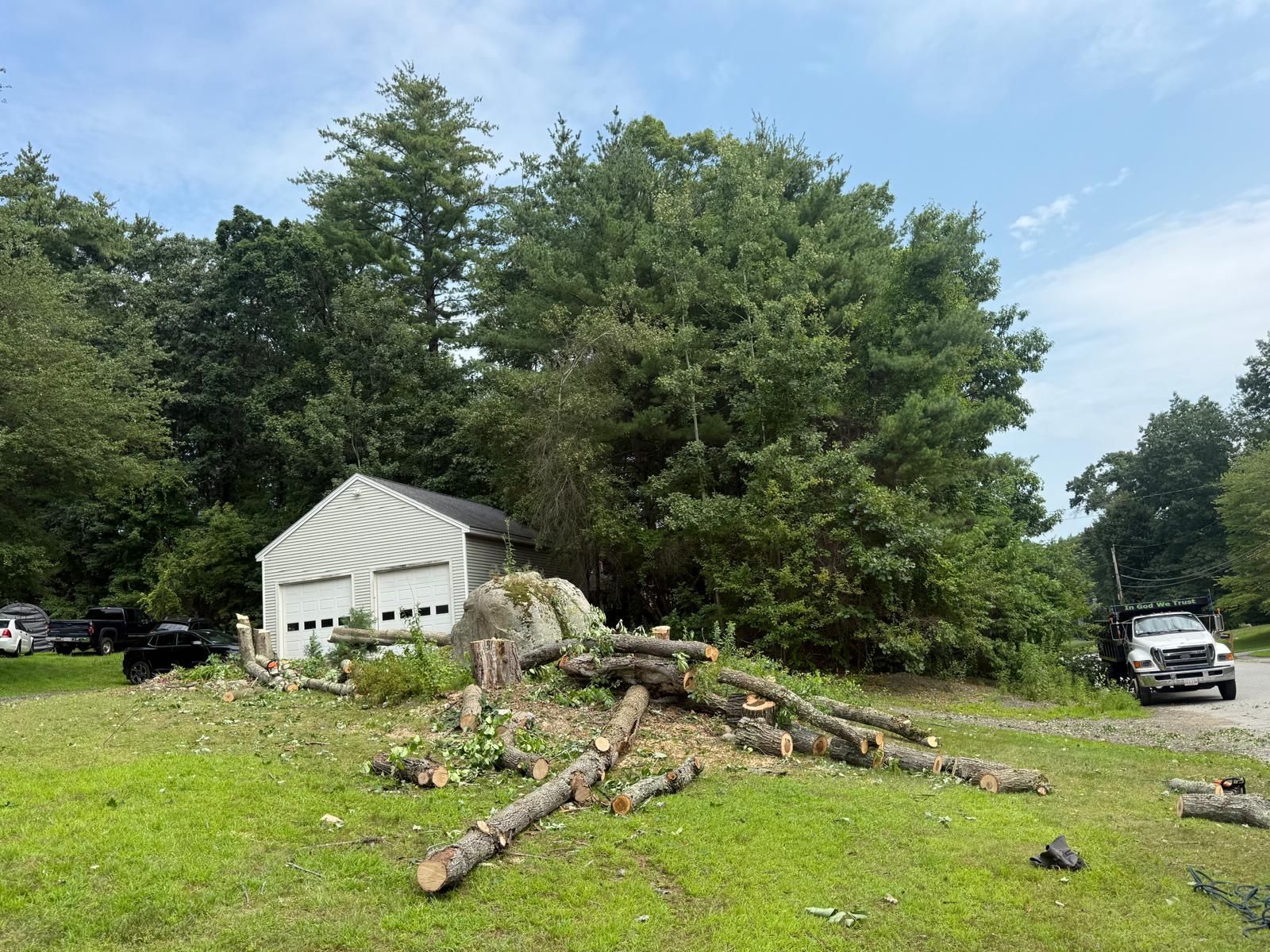 Storm-damaged tree limbs strewn across a grassy yard beside a white garage and parked cars