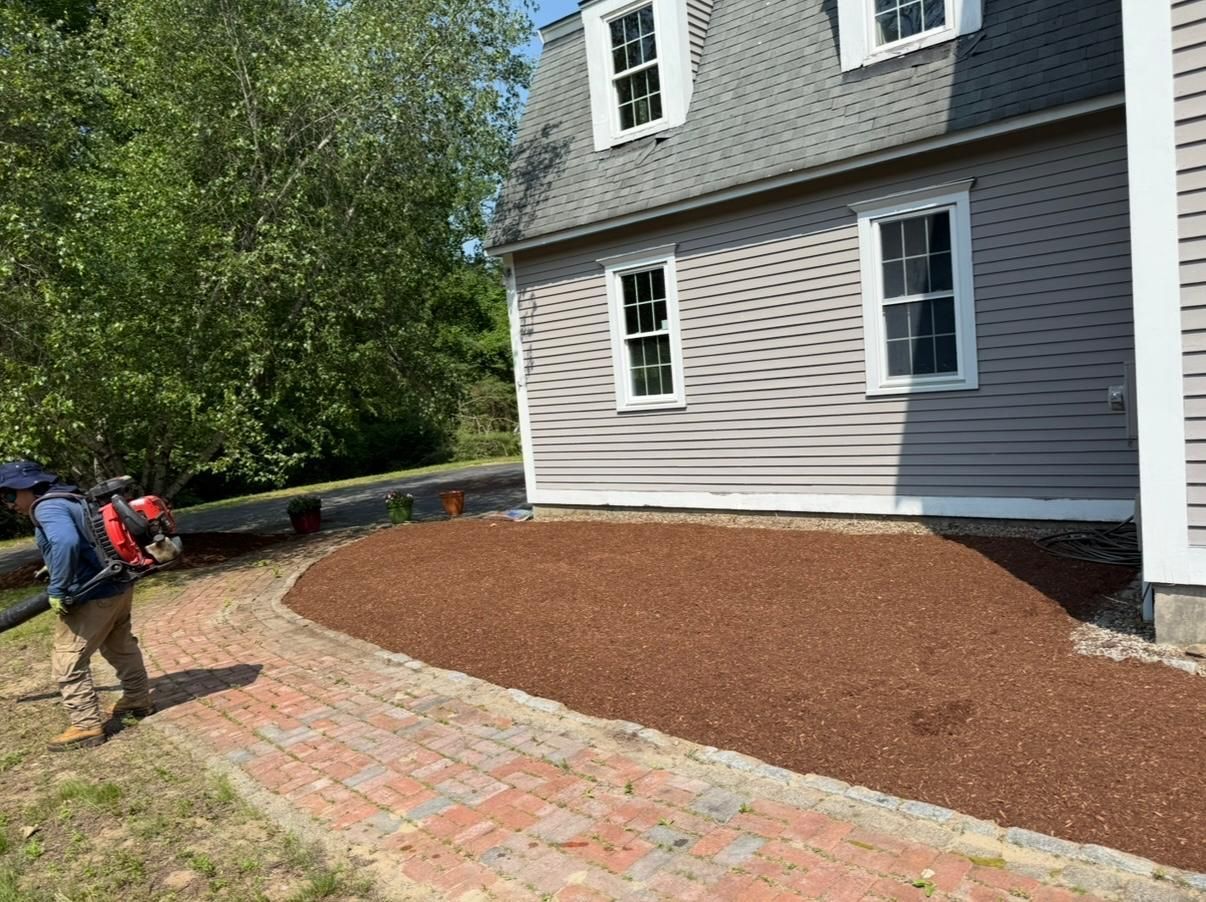 Person with backpack walking past a house beside a freshly mulched garden bed