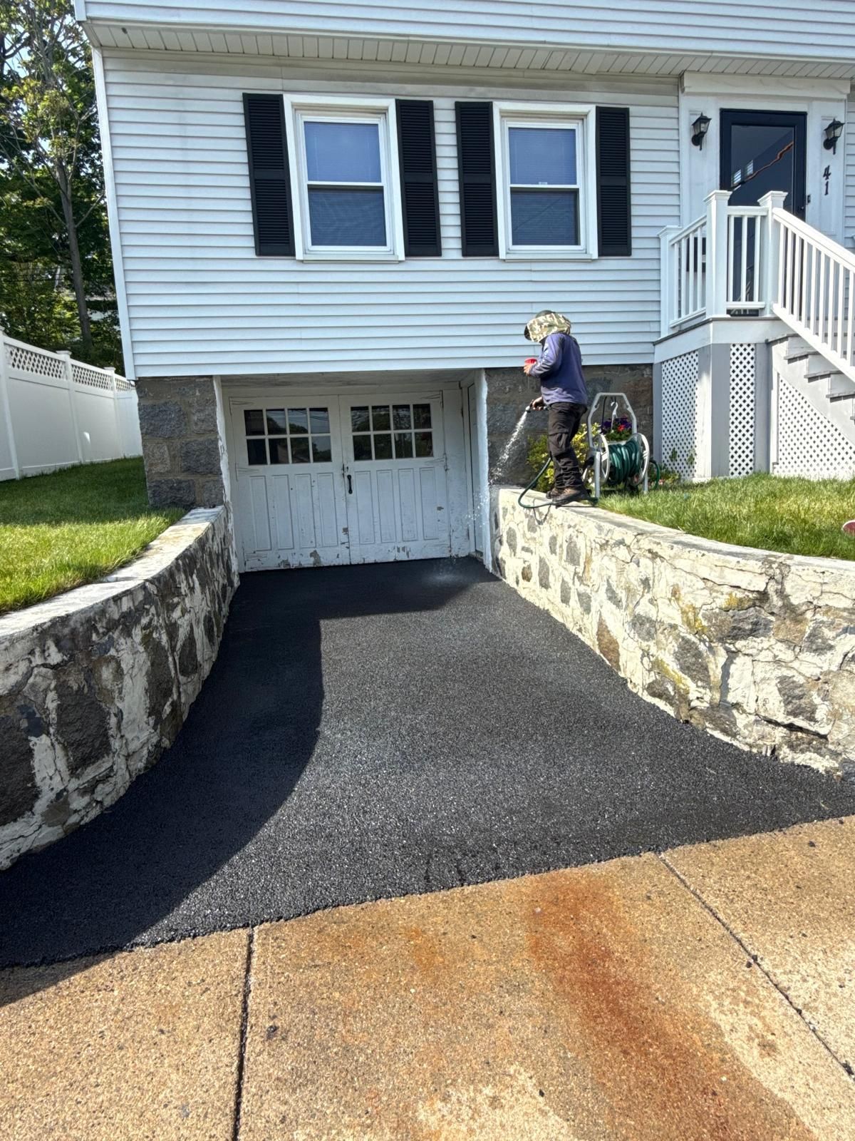 Fresh black asphalt driveway leading to a garage, with stone retaining walls and a house front entry.