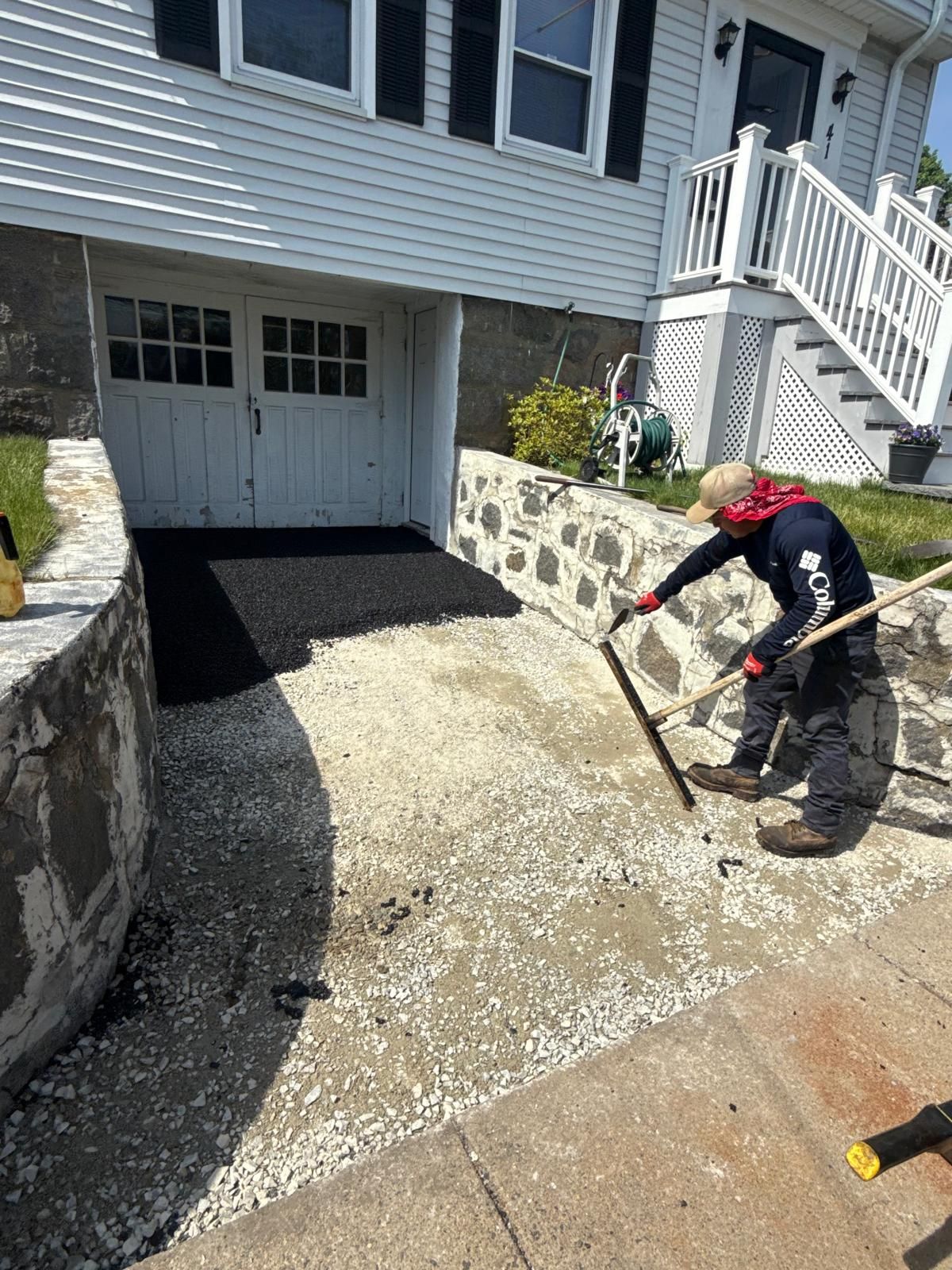 Worker leveling gravel driveway beside a white house and garage