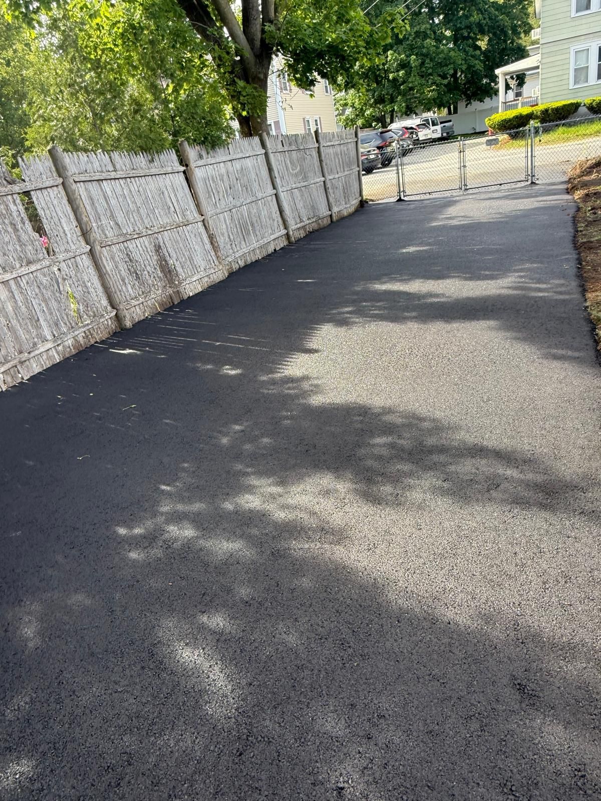 Shaded paved path beside a white fence and trees on a sunny day