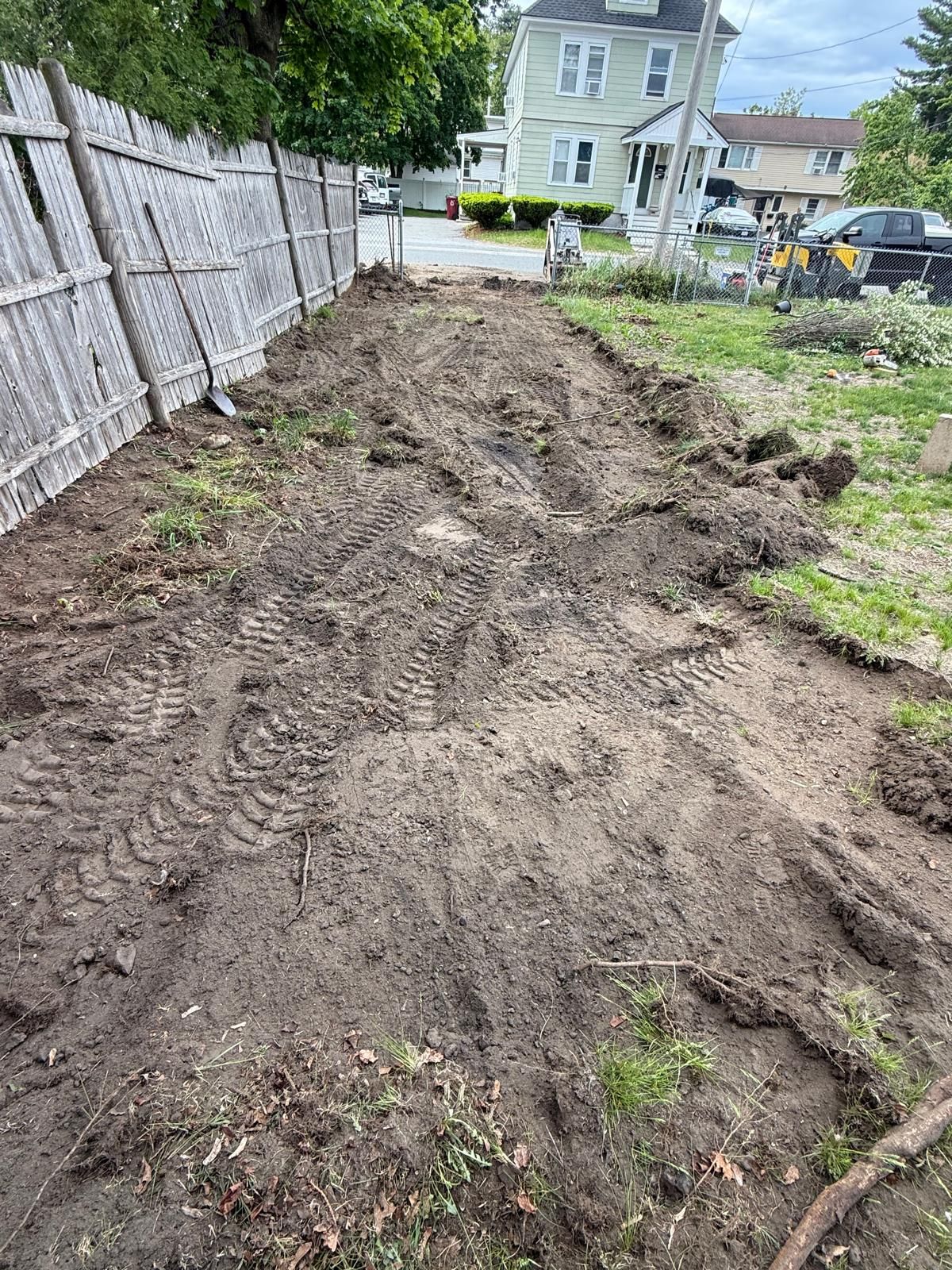 Freshly dug backyard soil beside a fence, with houses and a parked car in the background.
