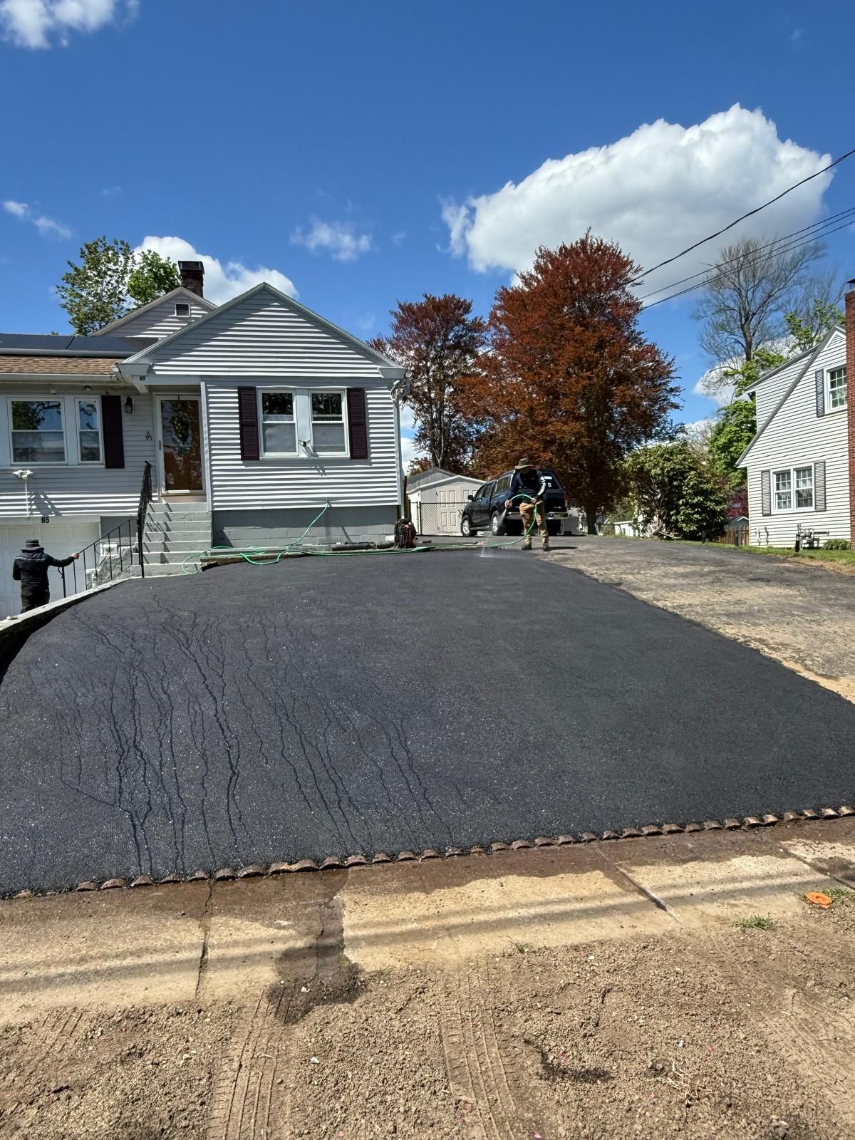 Freshly paved black driveway in front of a gray house on a sunny day