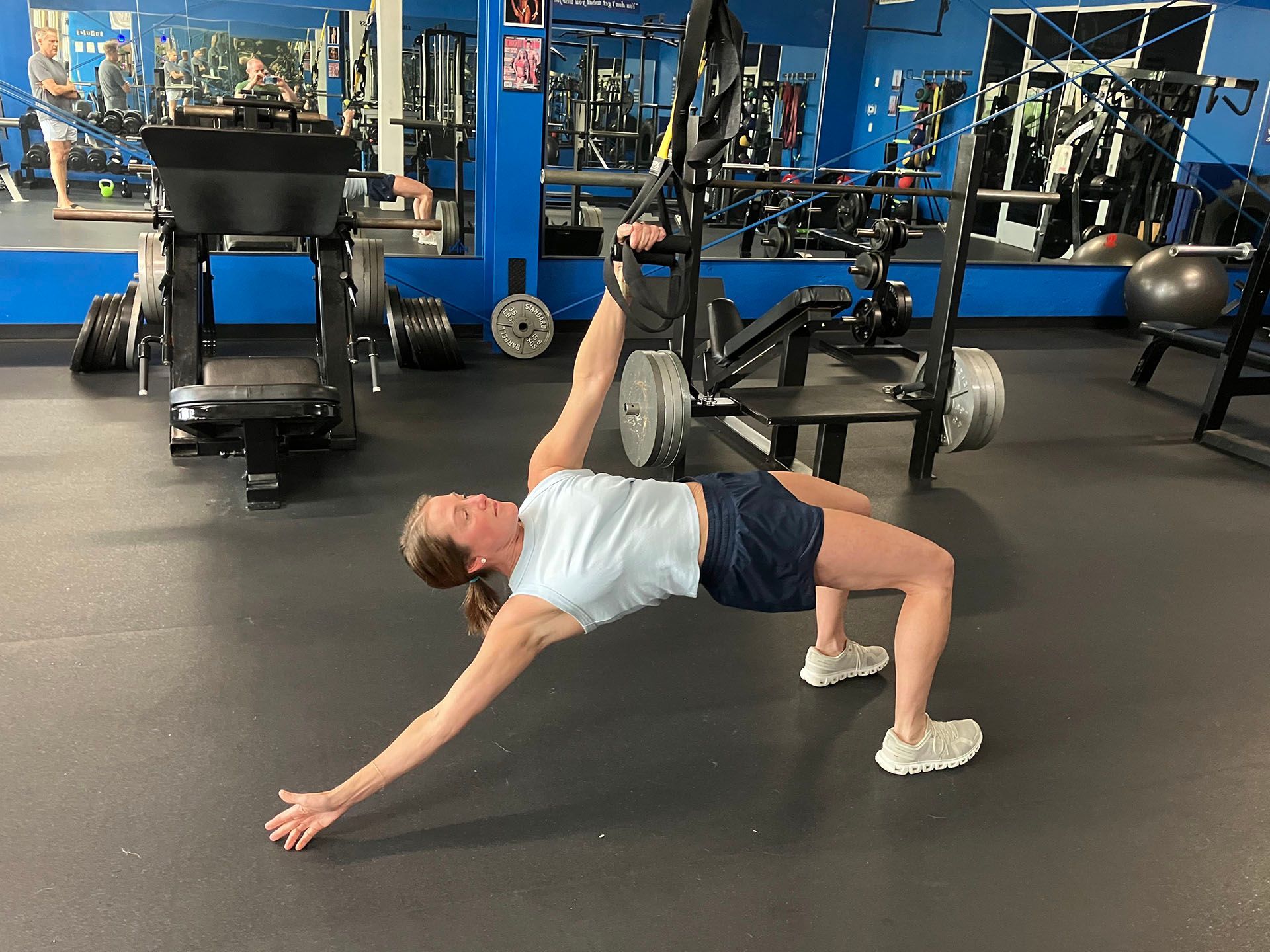 Person doing a bridge stretch in a gym, with one arm extended and one leg lifted on a bench.