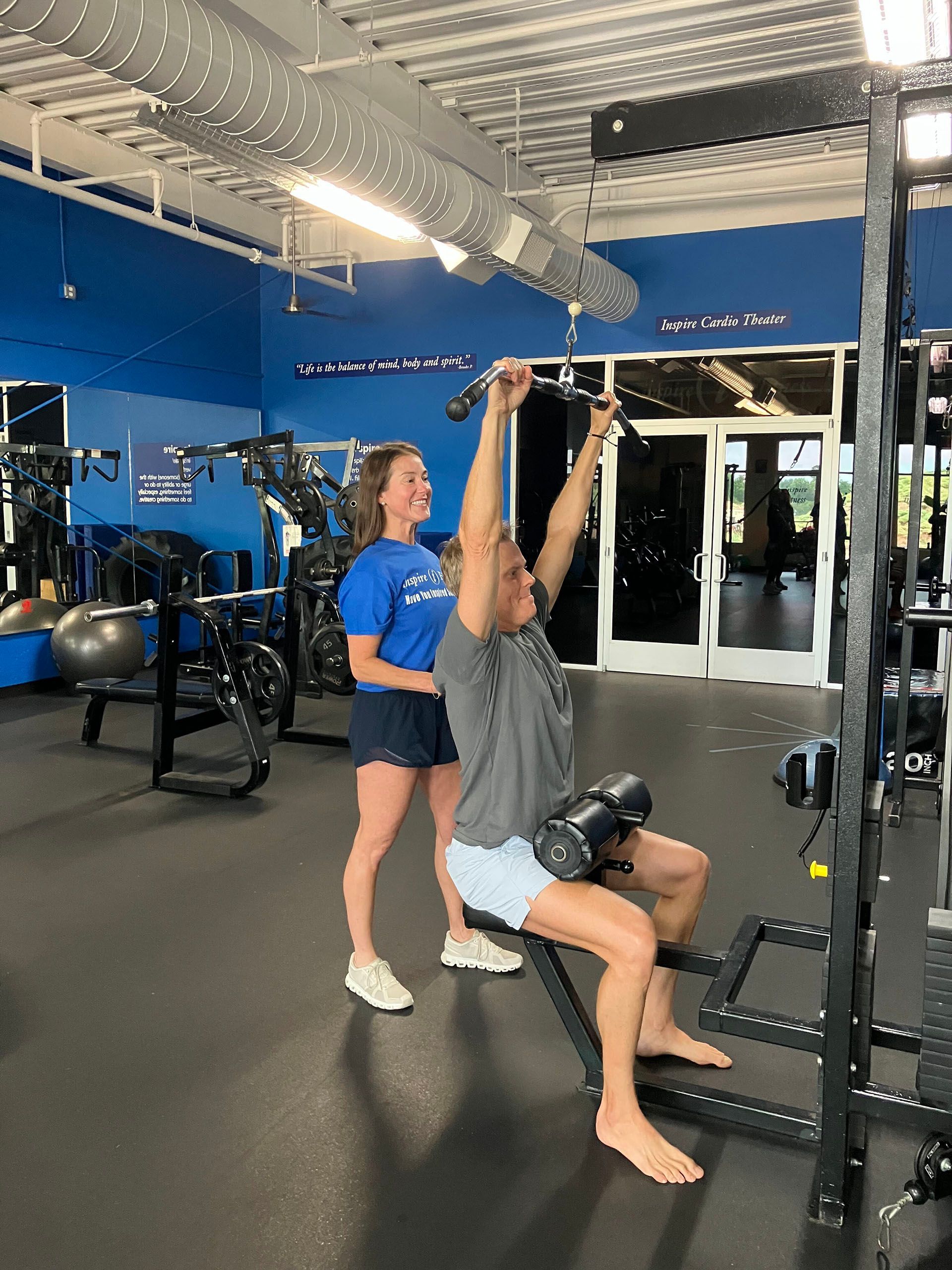 Trainer assisting client with lat pulldown exercise in a gym.