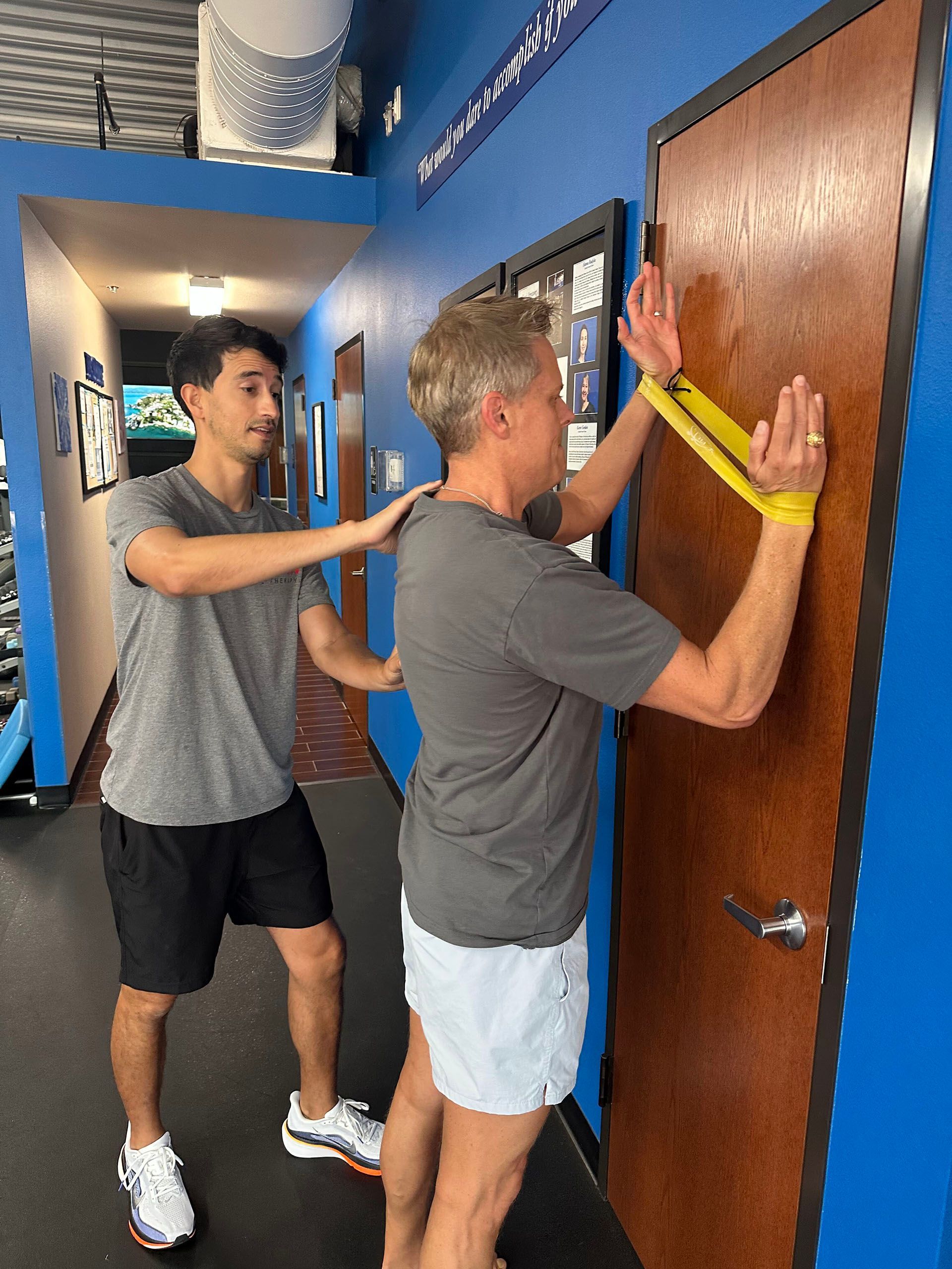 Two men measuring a doorway in a hallway with a yellow tape measure.