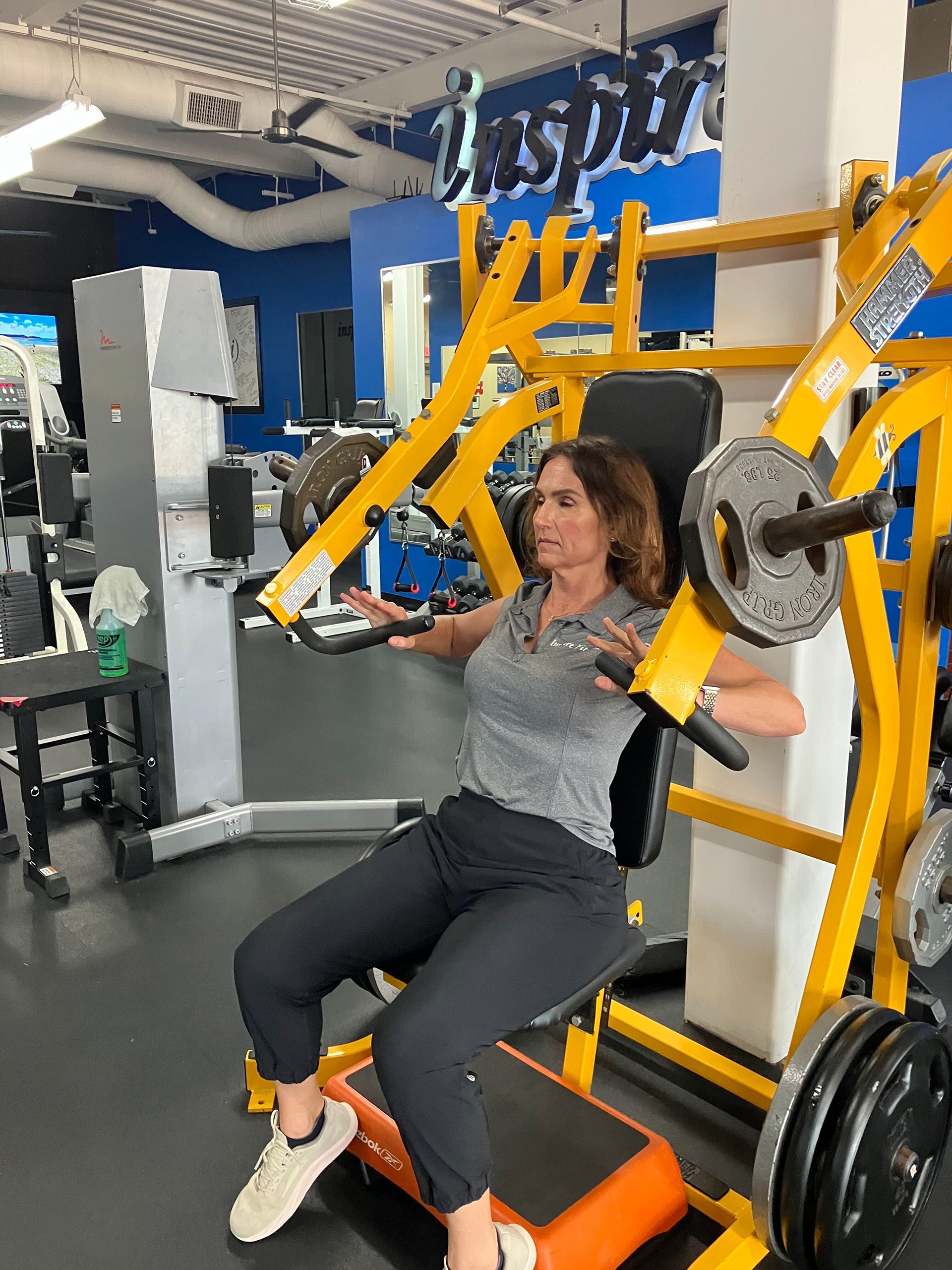 Person using a seated weight machine in a gym, holding handles with yellow frame and black plates.
