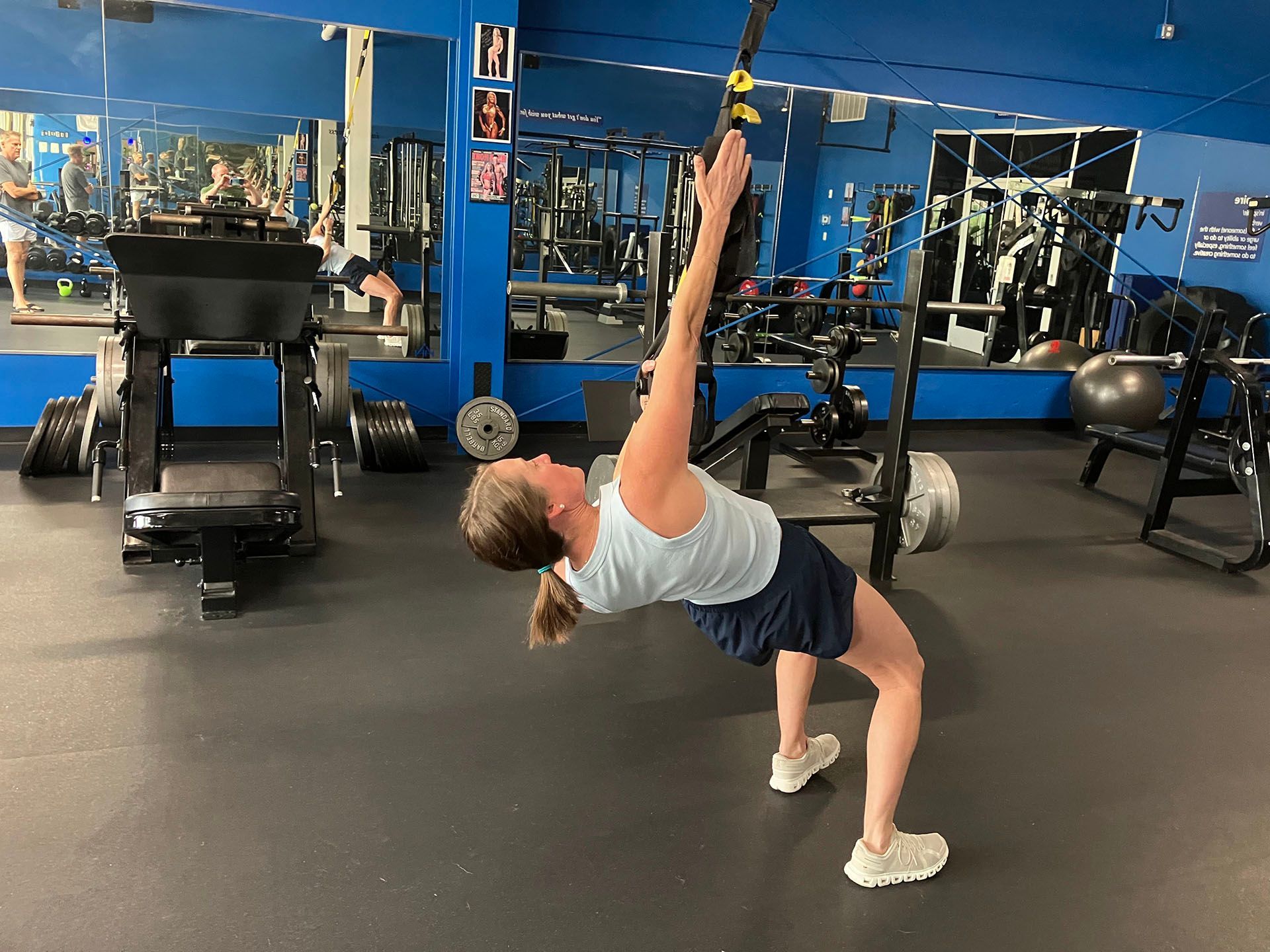 Person doing a backbend stretch in a blue gym, with workout equipment in the background.