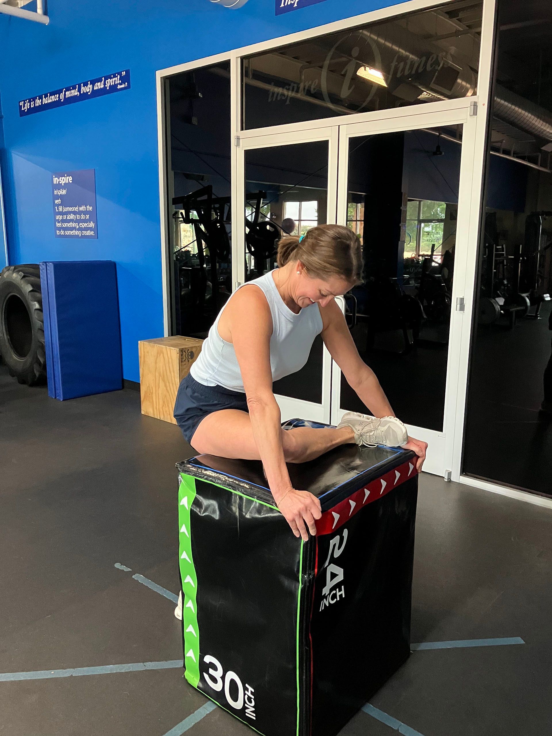 Person leaning on a black plyometric box in a gym, preparing to exercise.