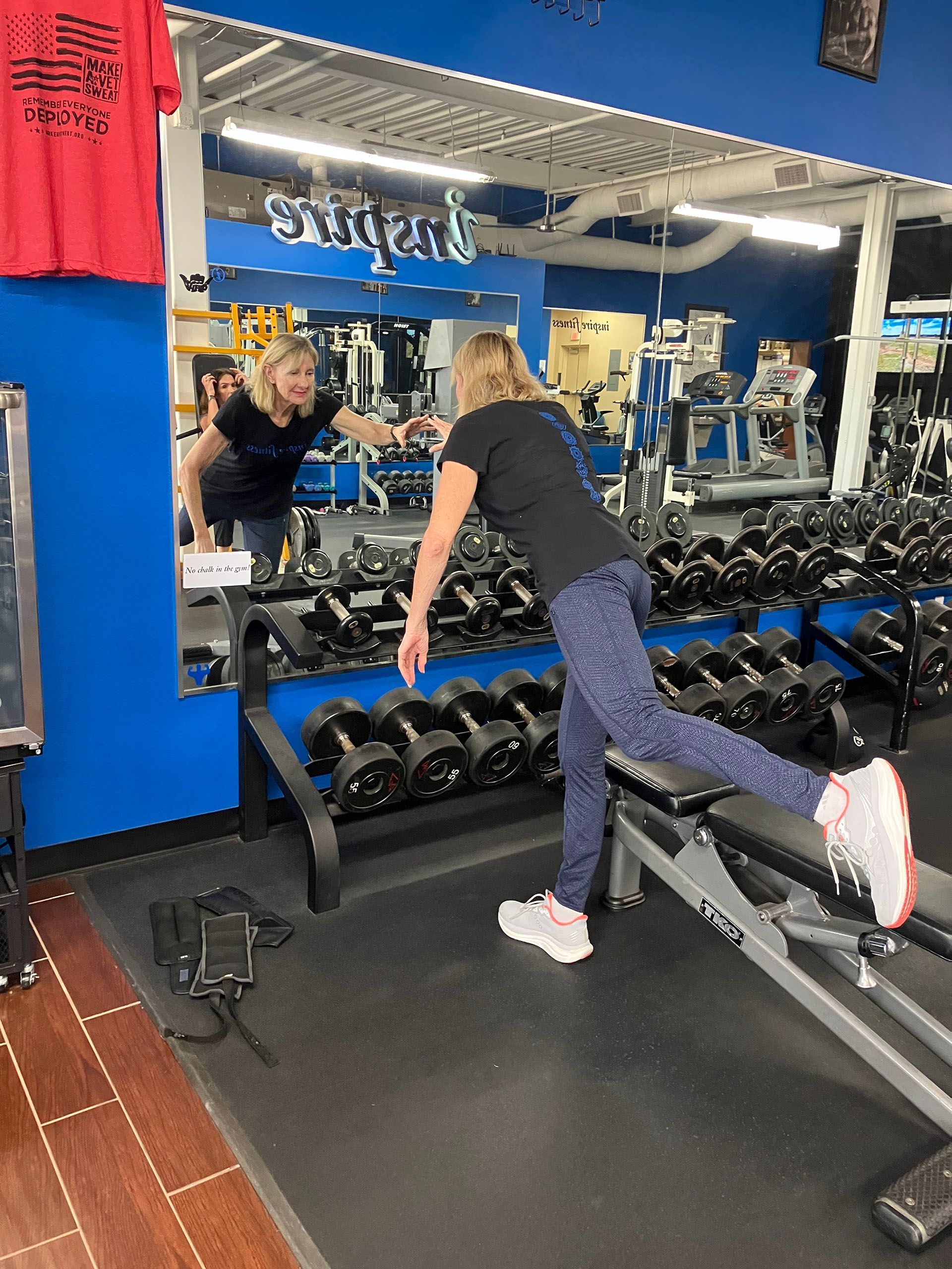 Person stretching on a bench in a gym, with dumbbells, mirrors, and a blue wall behind.