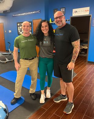 Three people smiling in a gym two men and a woman. The woman stands in between them.
