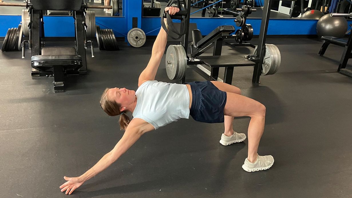 Person doing a bridge stretch in a gym, one leg raised on a bench, arms extended on the floor.