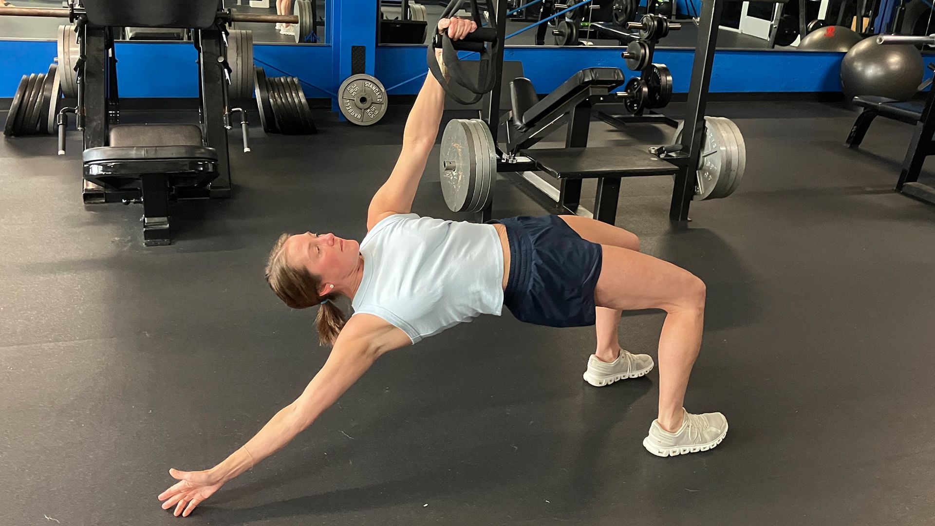 Person doing a bridge stretch in a gym, one leg raised on a bench, arms extended on the floor.