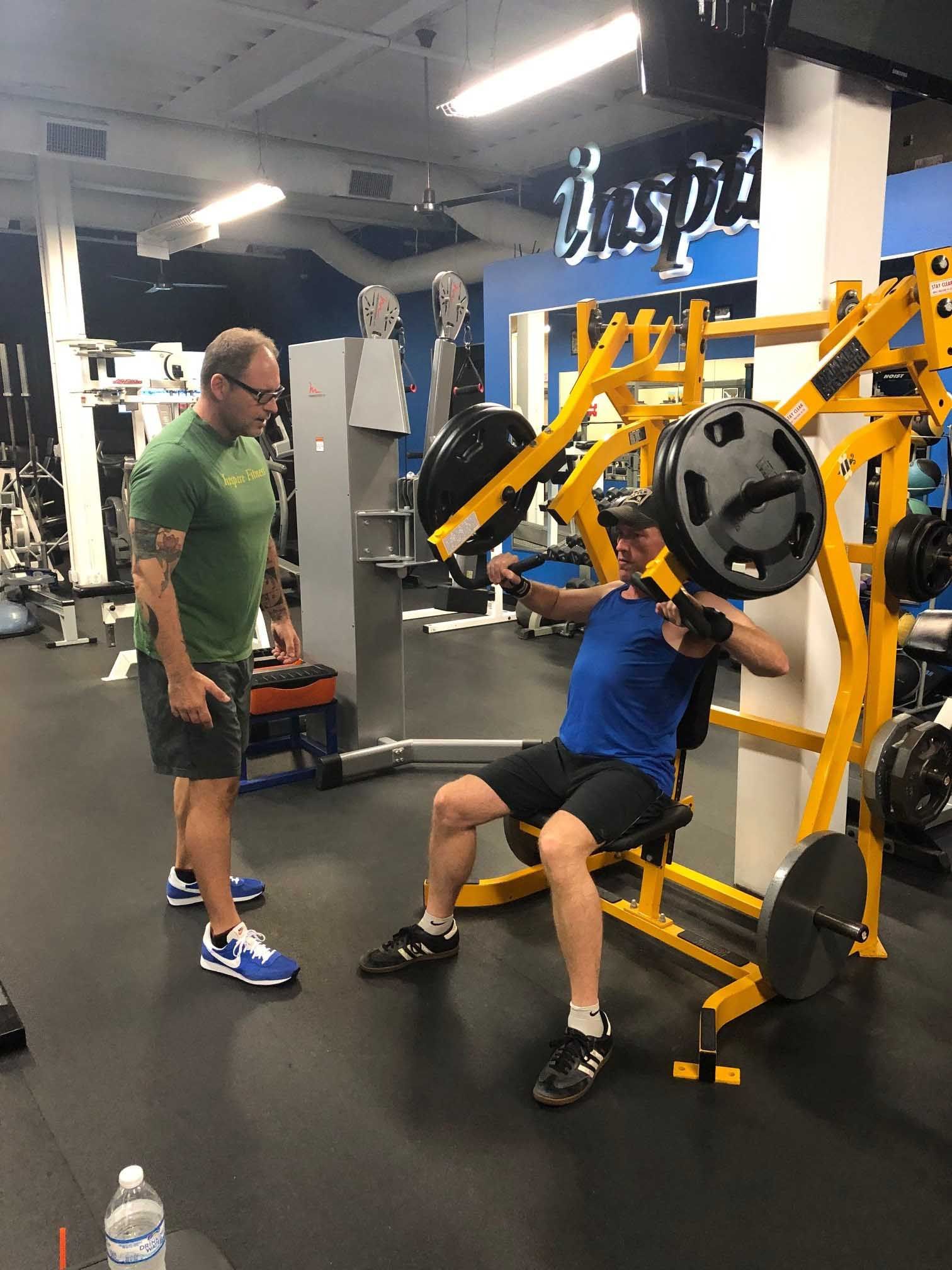 Man exercising on a weight machine with a trainer in a gym.