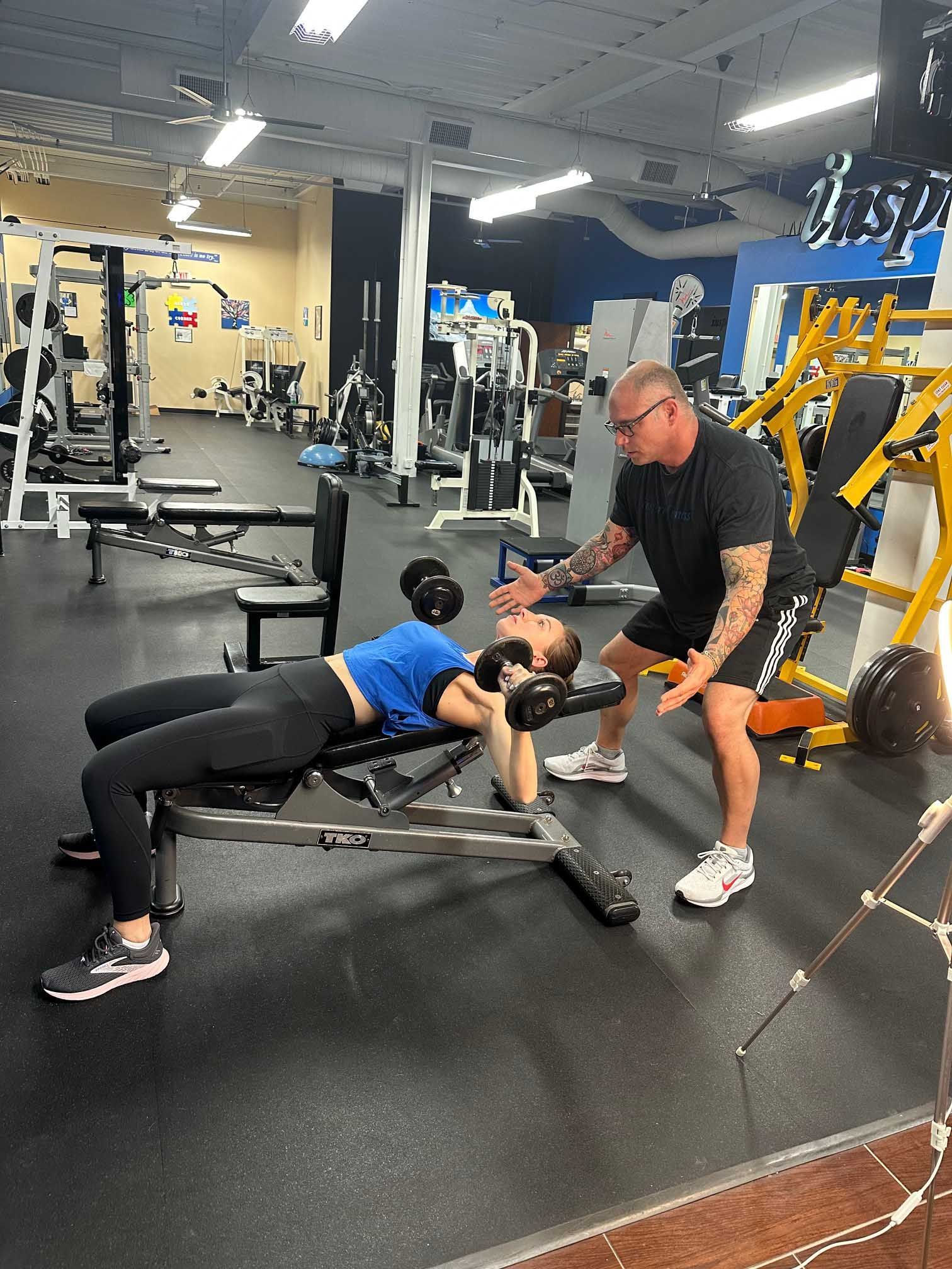 Woman doing dumbbell chest press with trainer in gym.
