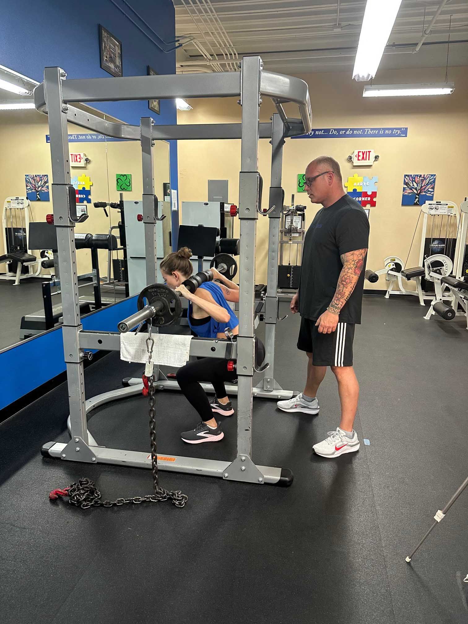 Woman squats with barbell in gym, trainer spotter.