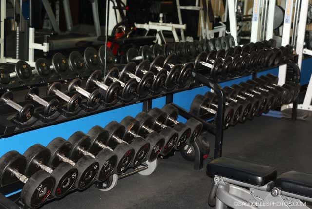 Rows of dumbbells on racks in a gym, with a mirror reflecting them.