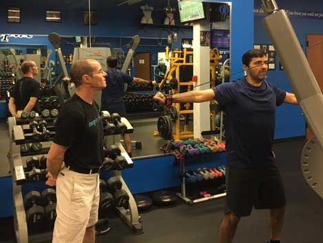 Man doing shoulder exercise with trainer at a gym.