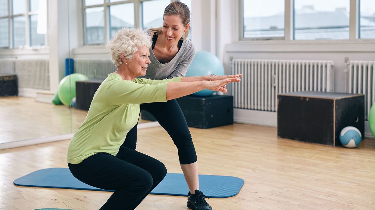 People in gym, exercise using resistance bands and stability balls. Instructor, two seniors, and one younger woman.