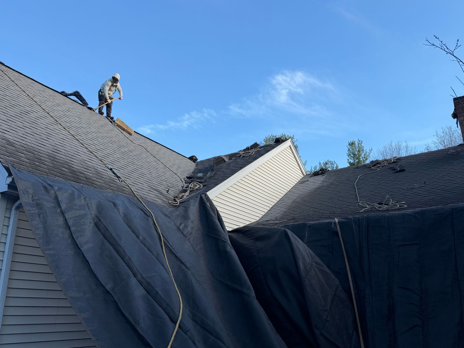 Worker on a shingled roof near a large white vent under a blue sky