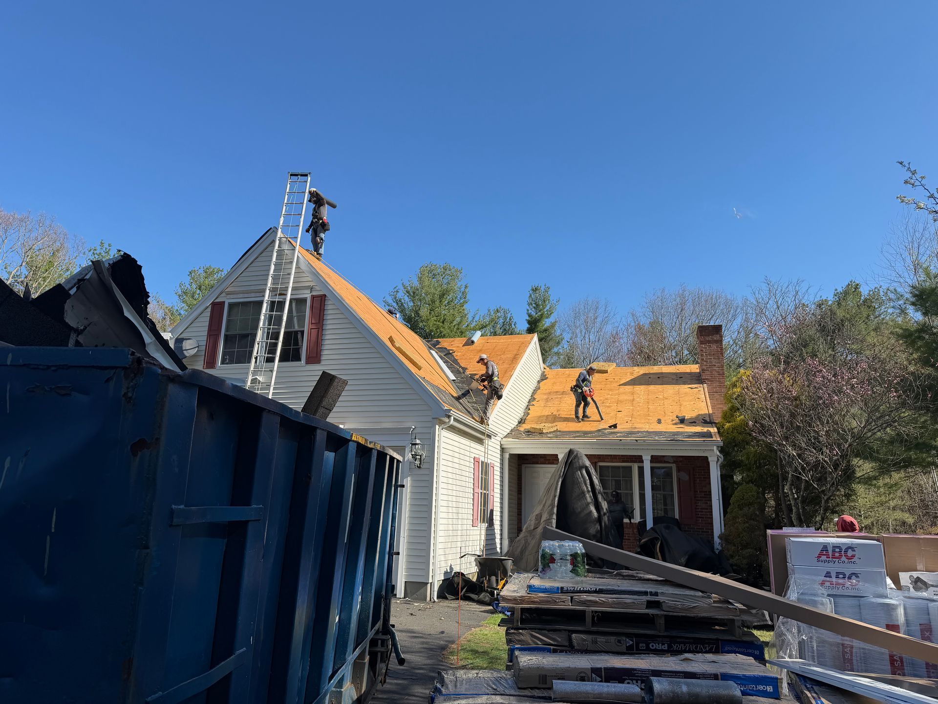 Partially renovated house with orange roof, white siding, and blue dumpster in a sunny yard