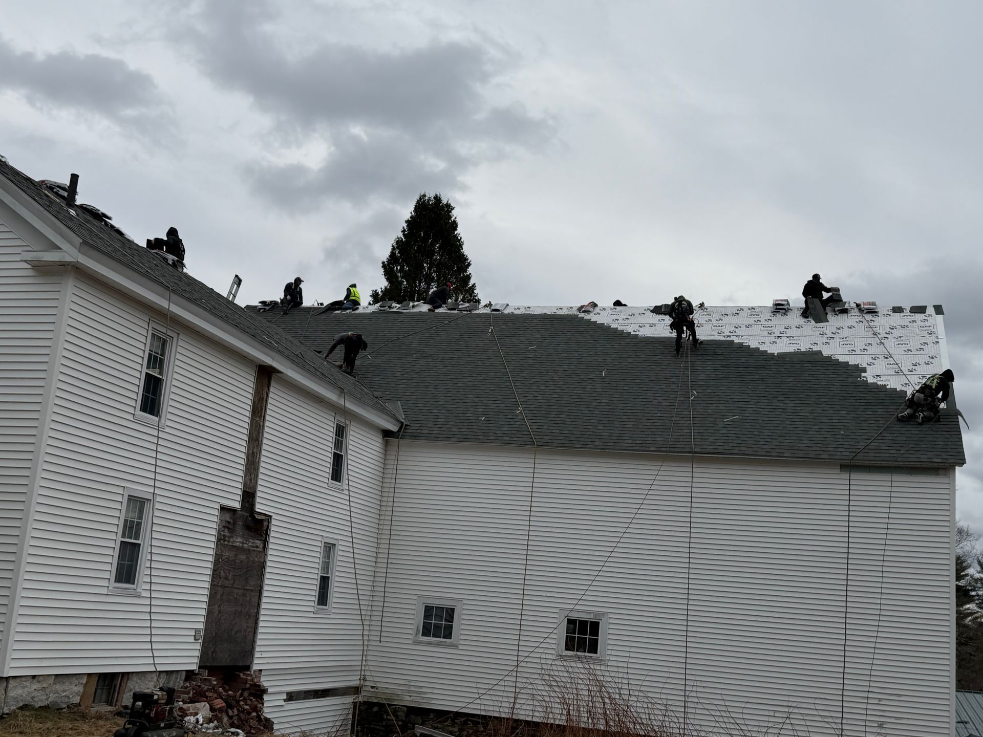 Snow-covered roof with several people working along the ridge on a white house