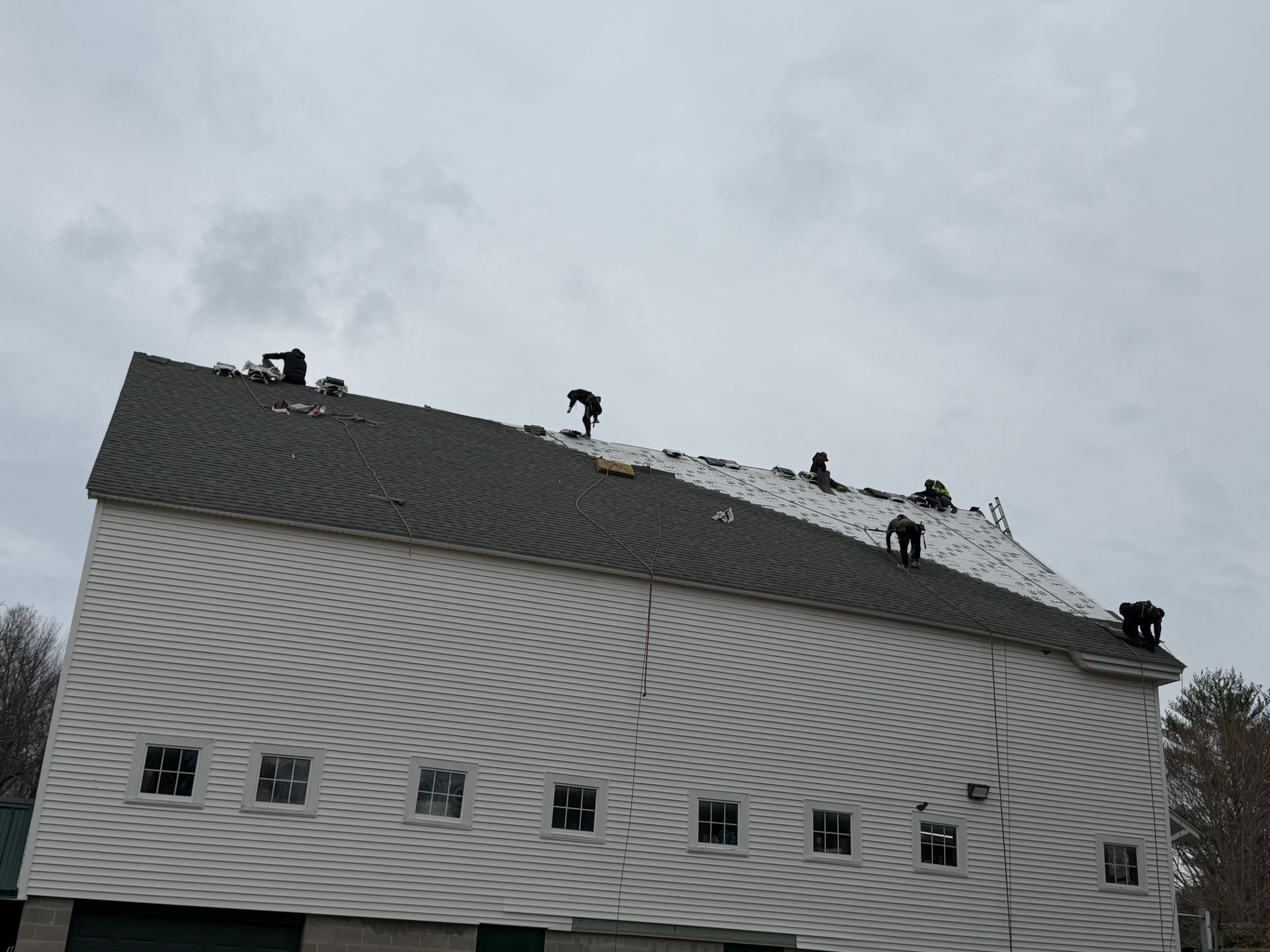 White house with a steep roof and several roofers working on top under a cloudy sky