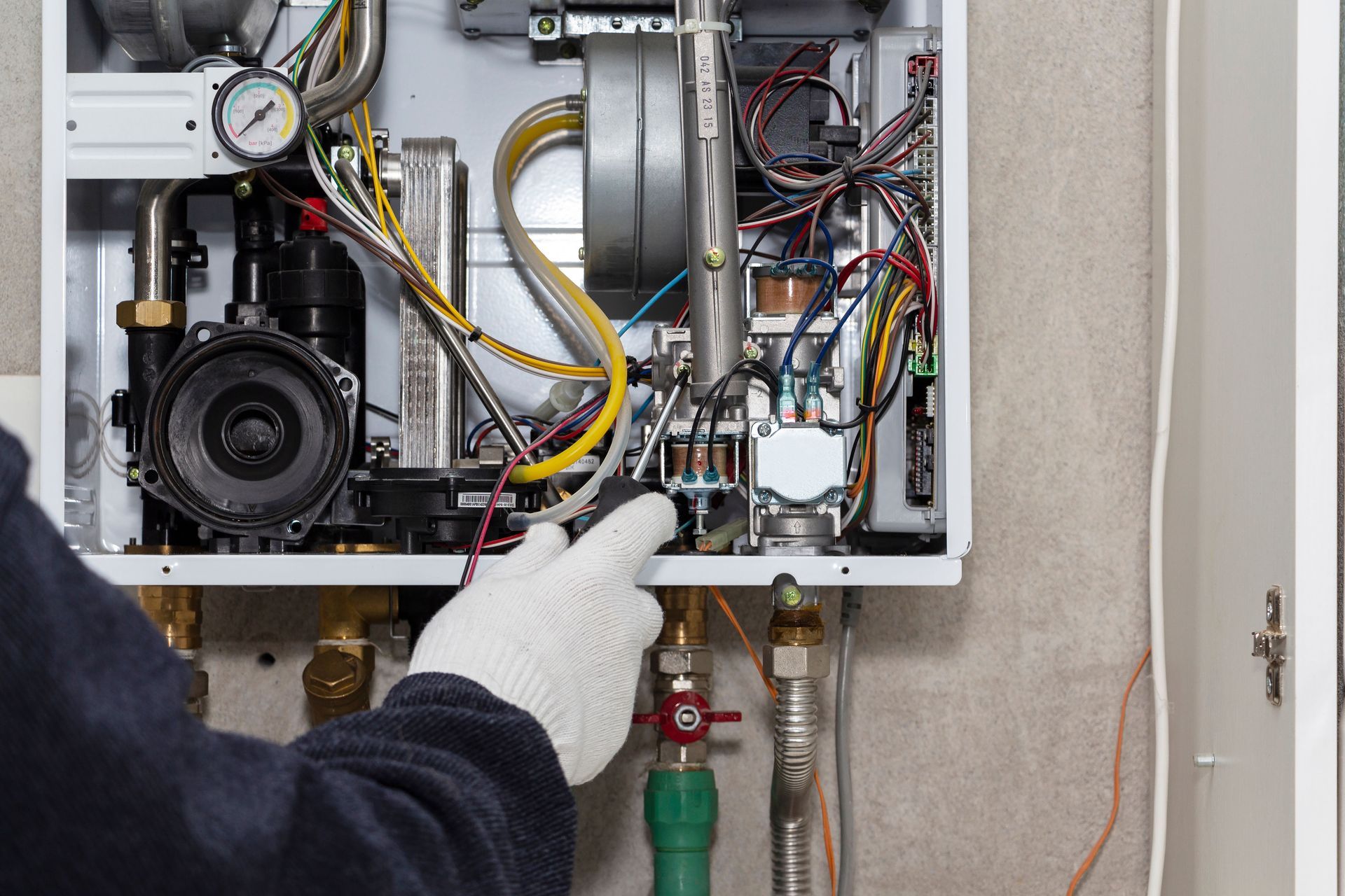 A technician wearing white gloves repairs the internal components of a wall-mounted gas boiler.