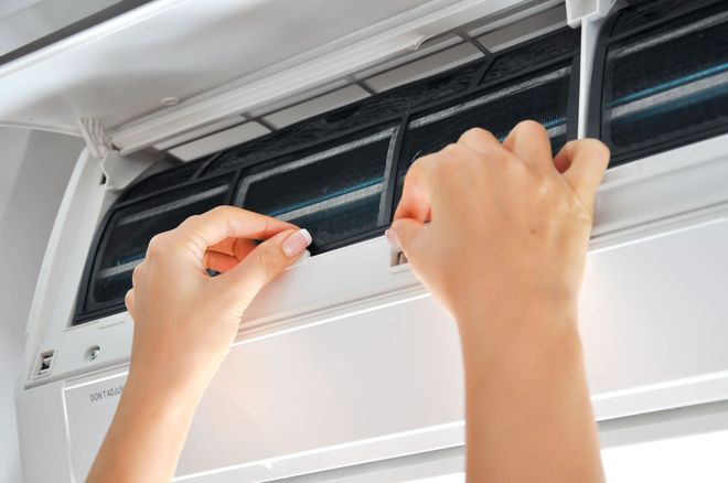 Hands removing a dust filter from an indoor wall-mounted air conditioning unit.