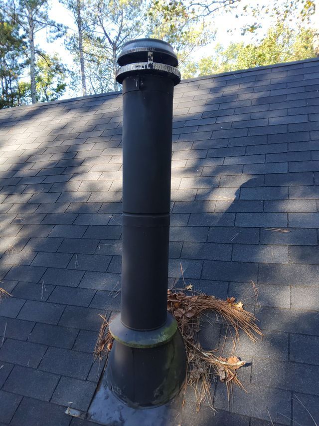 A black chimney on top of a roof with trees in the background.