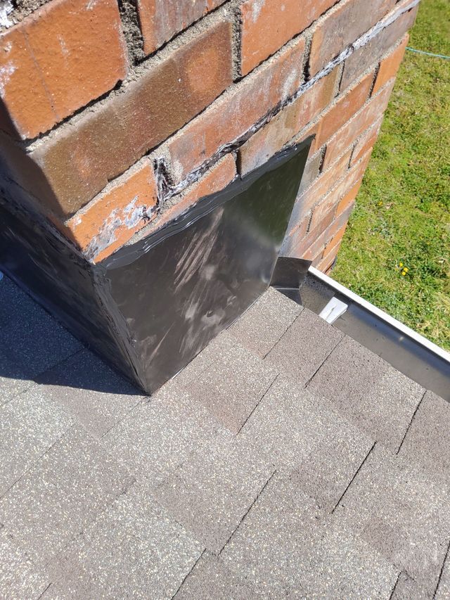 A brick chimney is sitting on top of a roof next to a gutter.